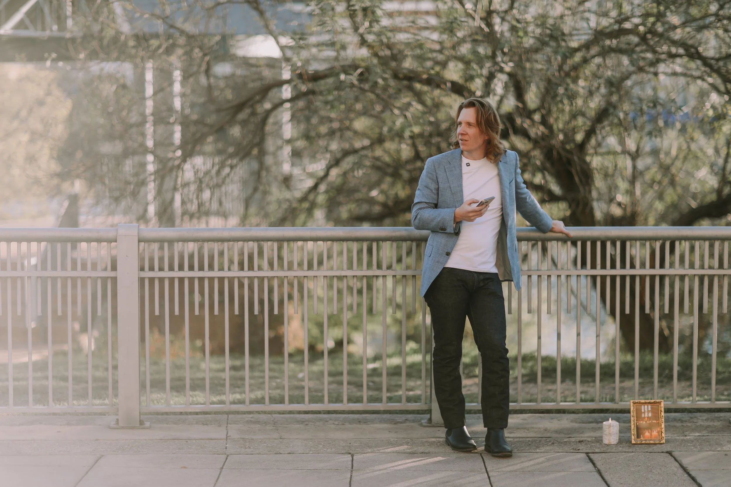 Jake waits alone at a lakeside railing with a small sign and candle before his surprise proposal in Austin, Texas