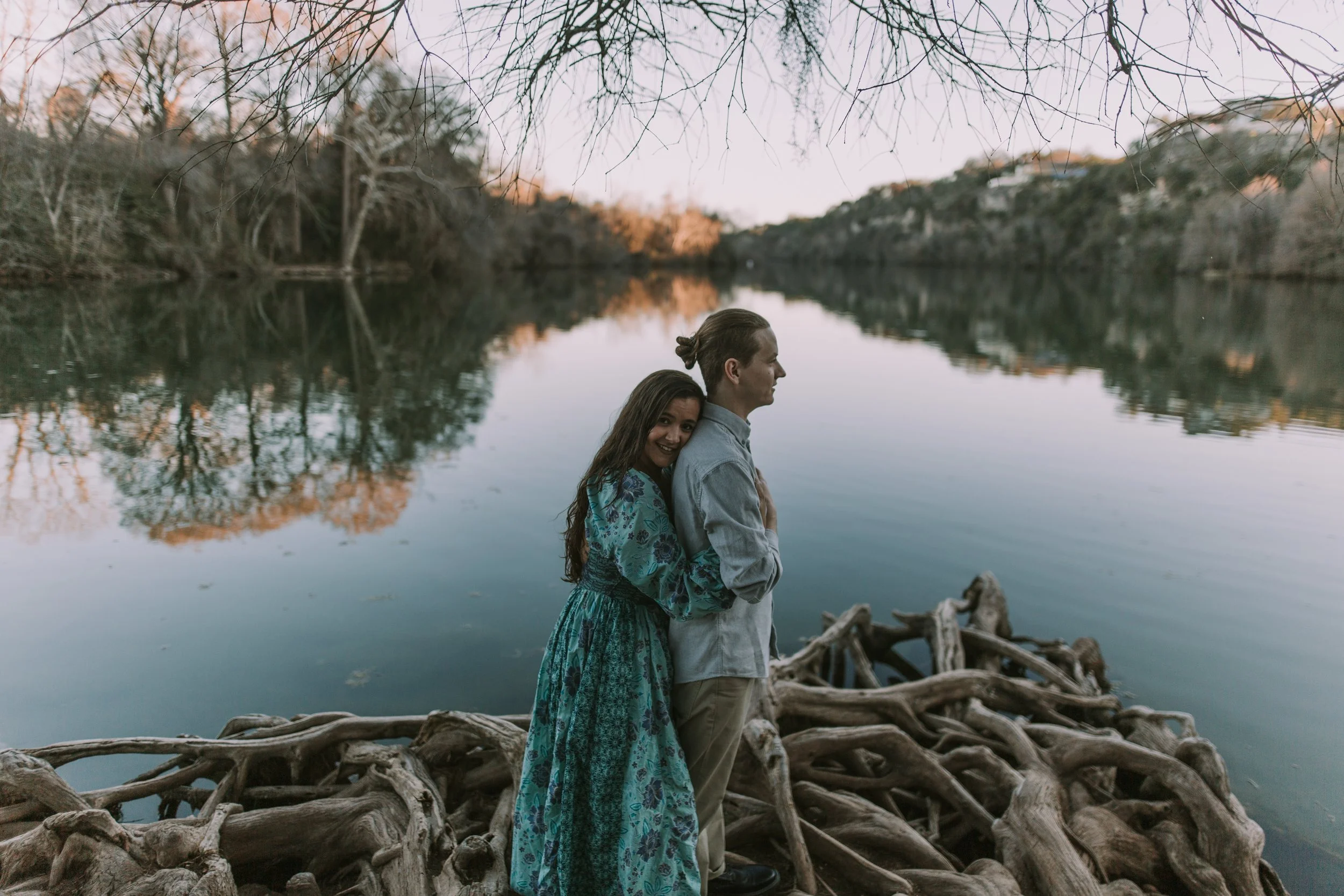 Jasmin and Grant on cypress roots at the edge of the Colorado River at dusk, Austin engagement session