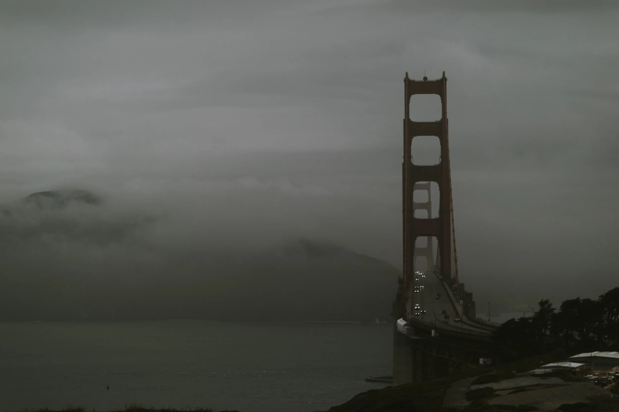 Golden Gate Bridge tower disappearing into fog with headlights crossing, San Francisco