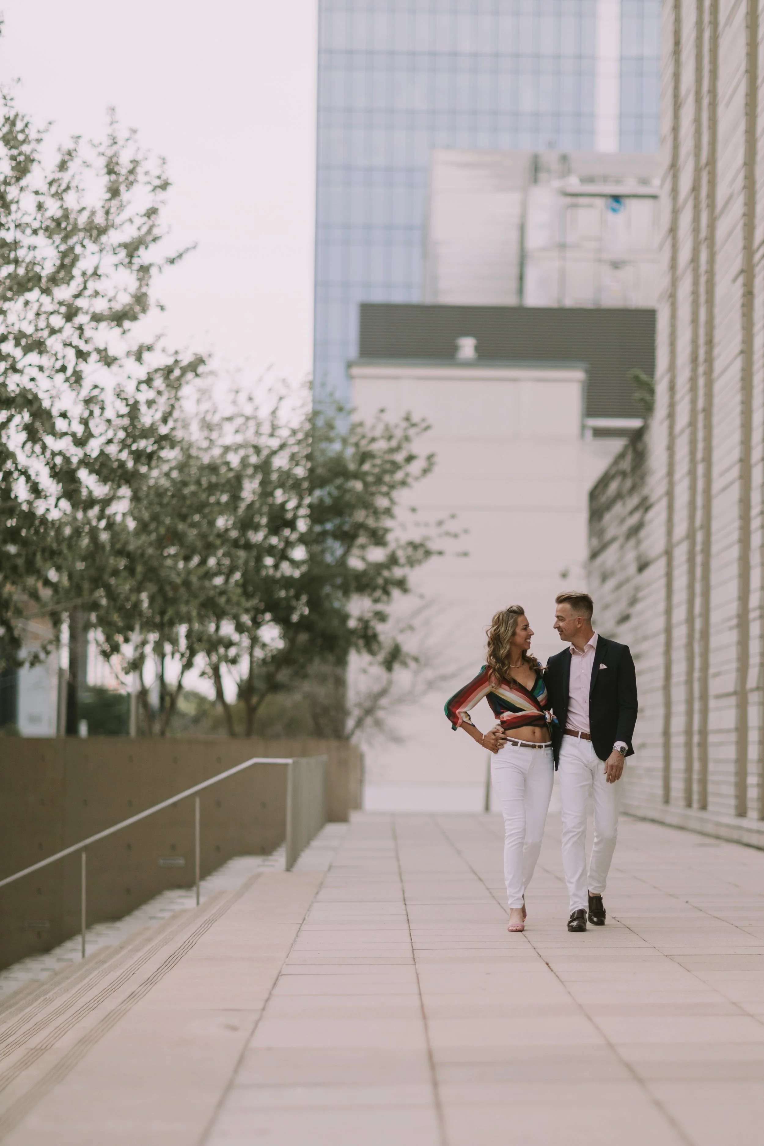 Couple walks a downtown Austin sidewalk between glass towers, dressed for the evening