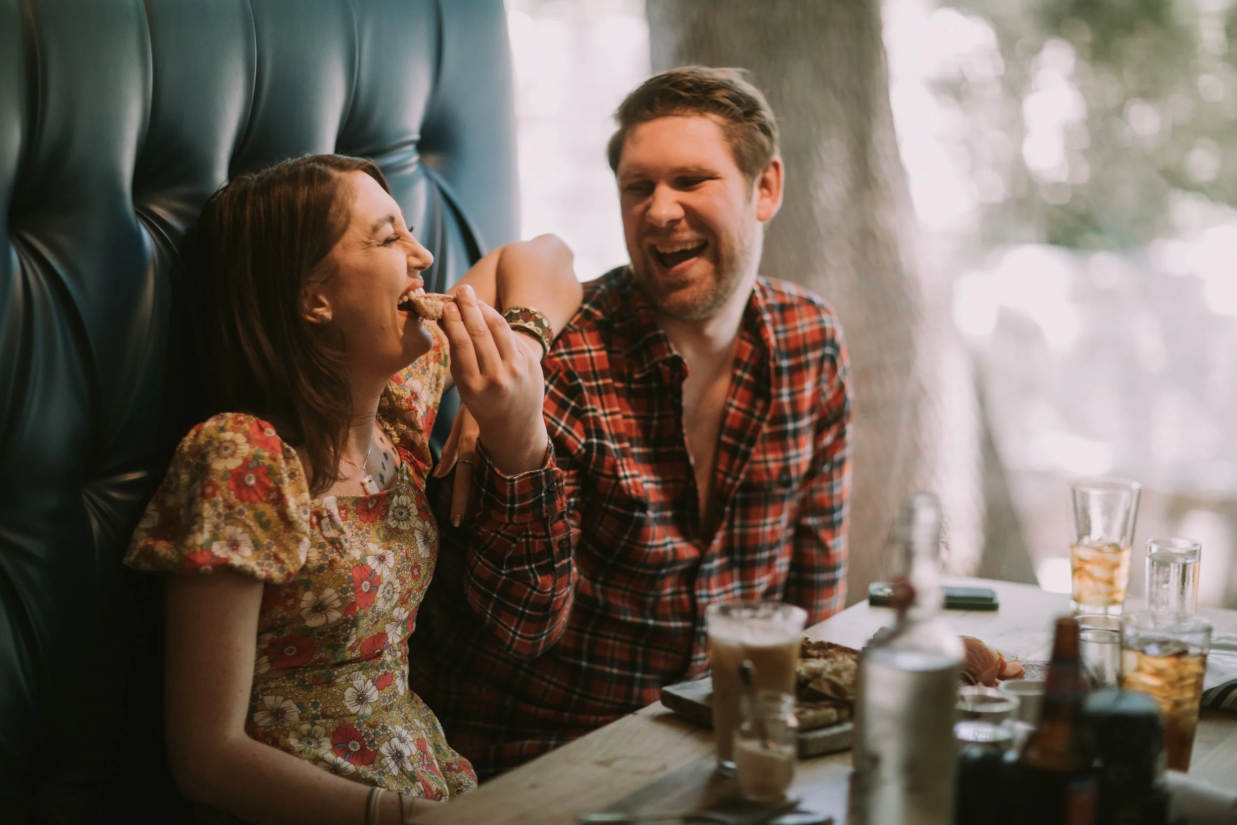 Molly and Shane laughing over cocktails and plates in a teal leather booth during their Austin engagement session