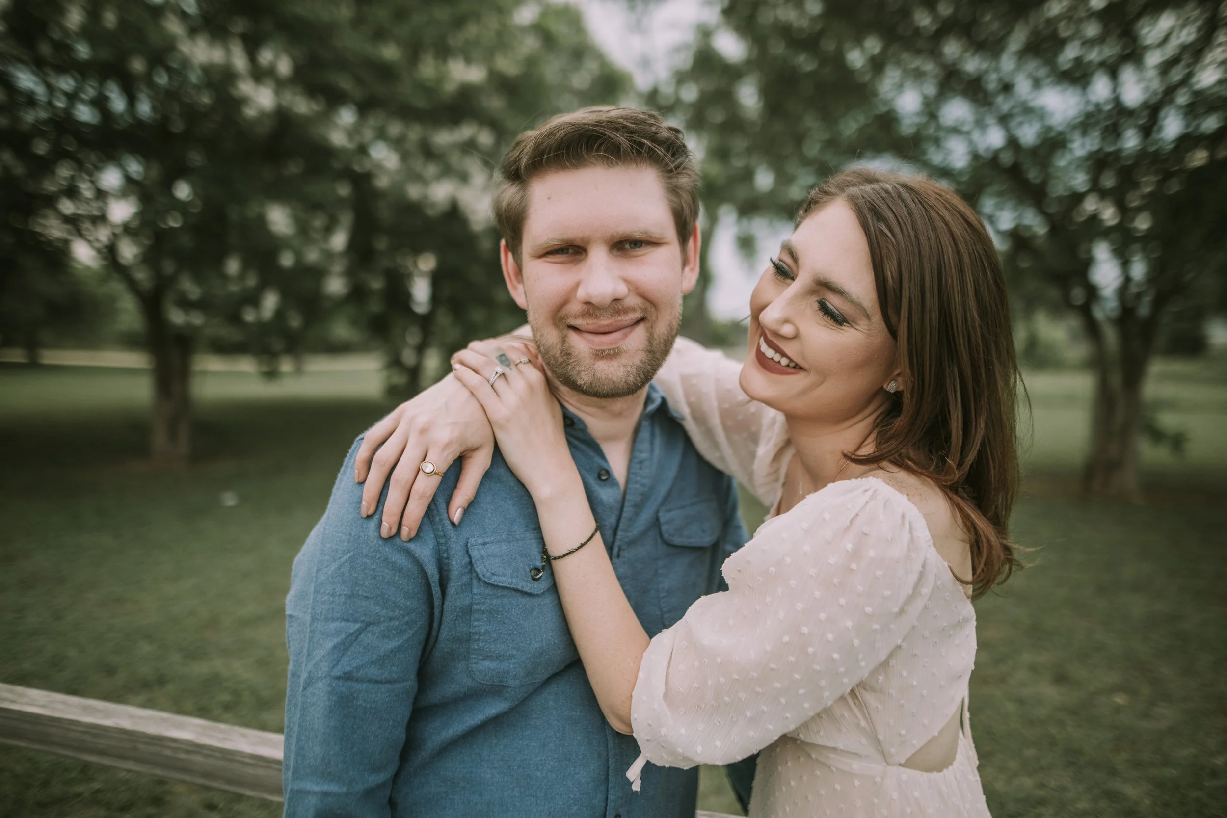 Engagement session under the trees in an Austin park, her arms around his shoulders