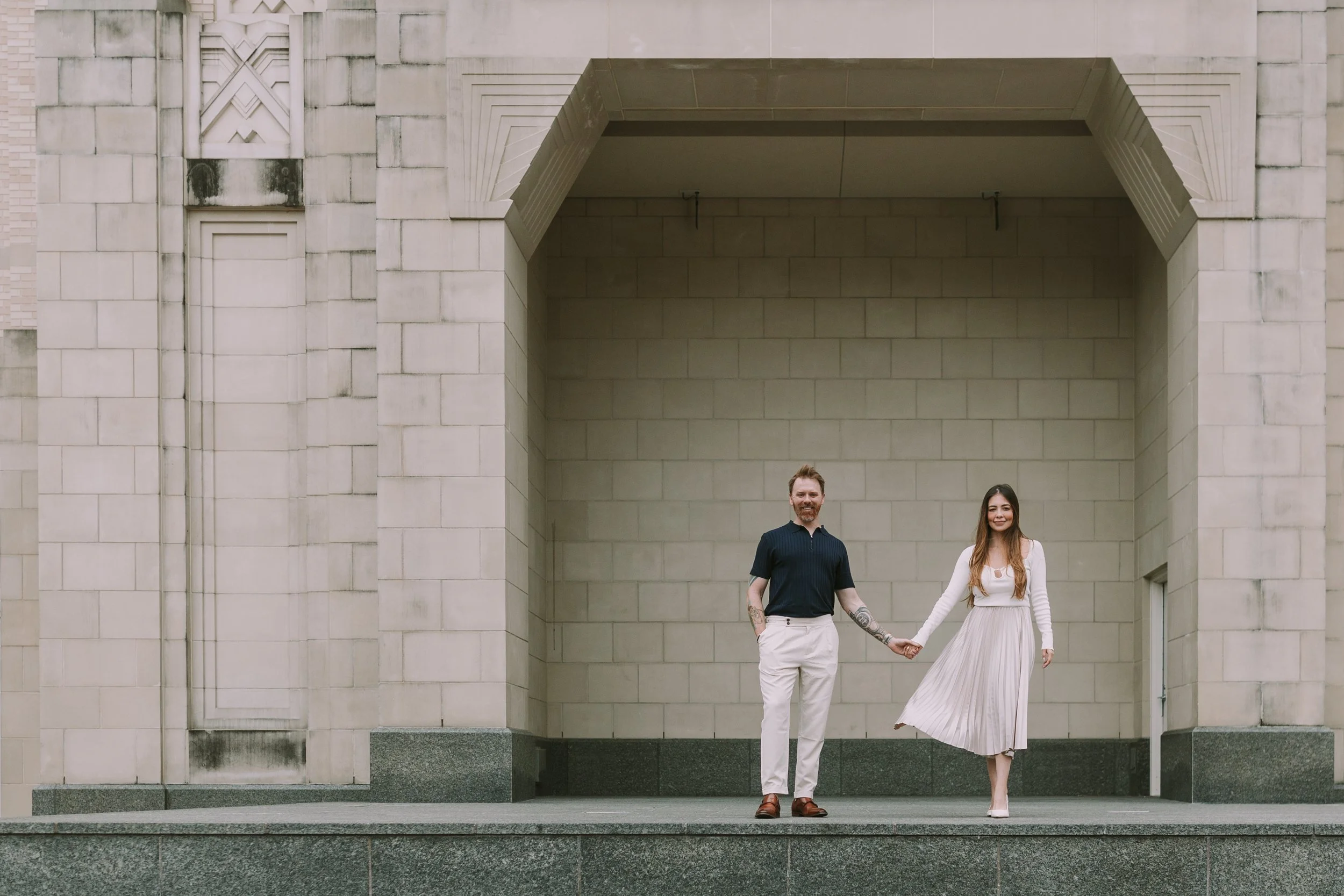 Sean and Maria holding hands beneath a grand art deco limestone archway in Sundance Square, Fort Worth